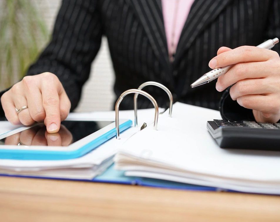 A person using a tablet and calculator on a desk.